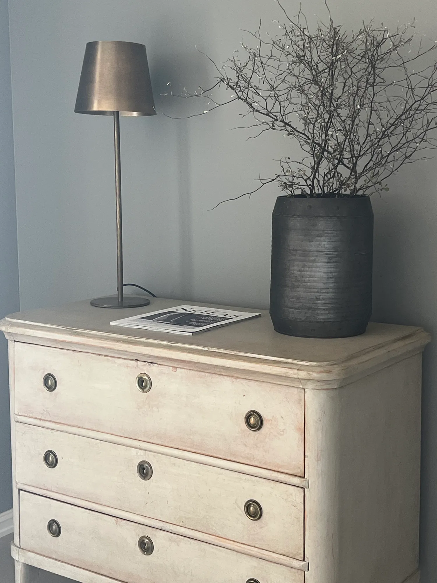 Lys, antikk kommode med lampe og krukke med grener