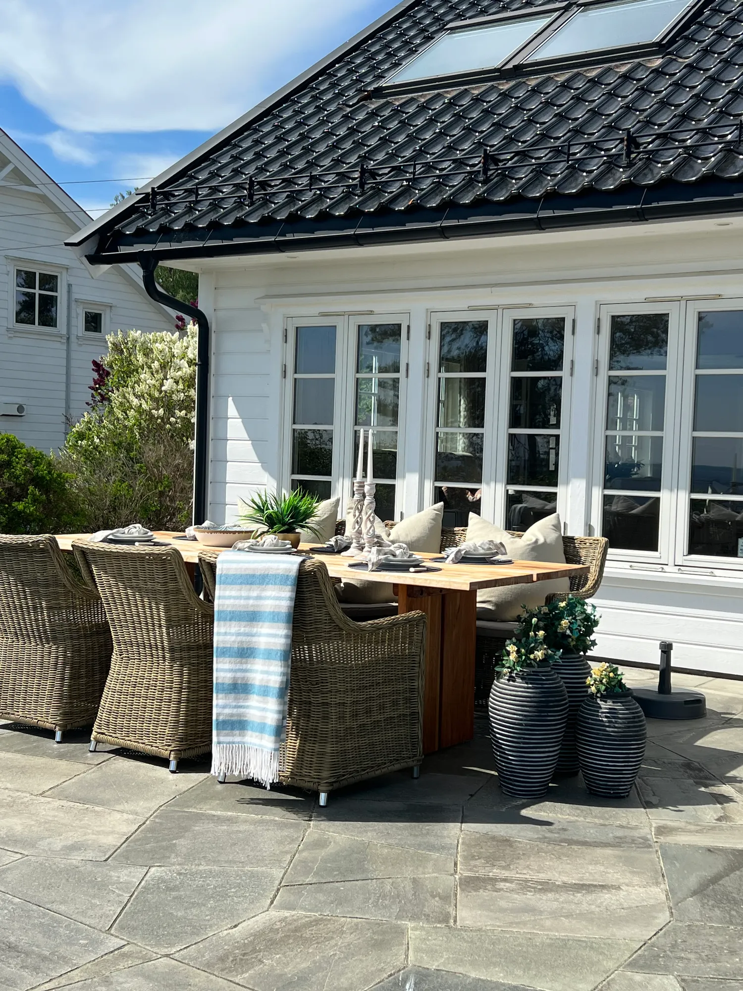 Terrasse med langbord og kurvstoler foran den hvite villaen