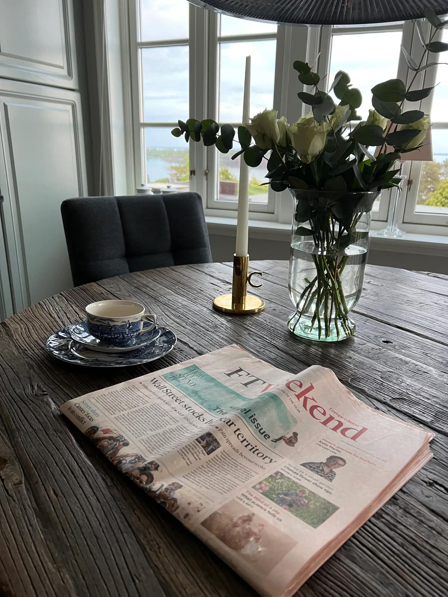 Frokostbord med avis, blå kopp og blomster i glassvase