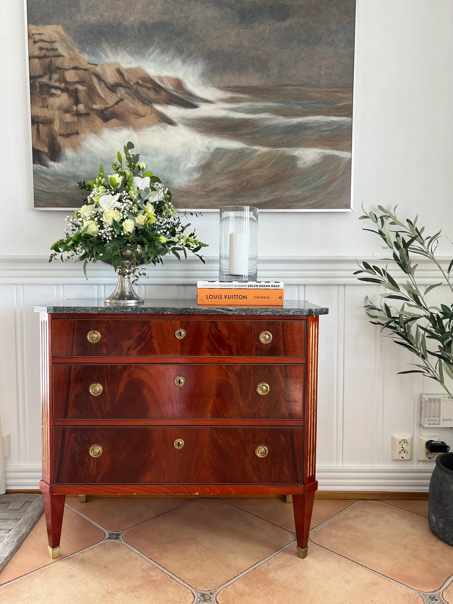 Antikk mahognikommode med blomster under et maleri av hav