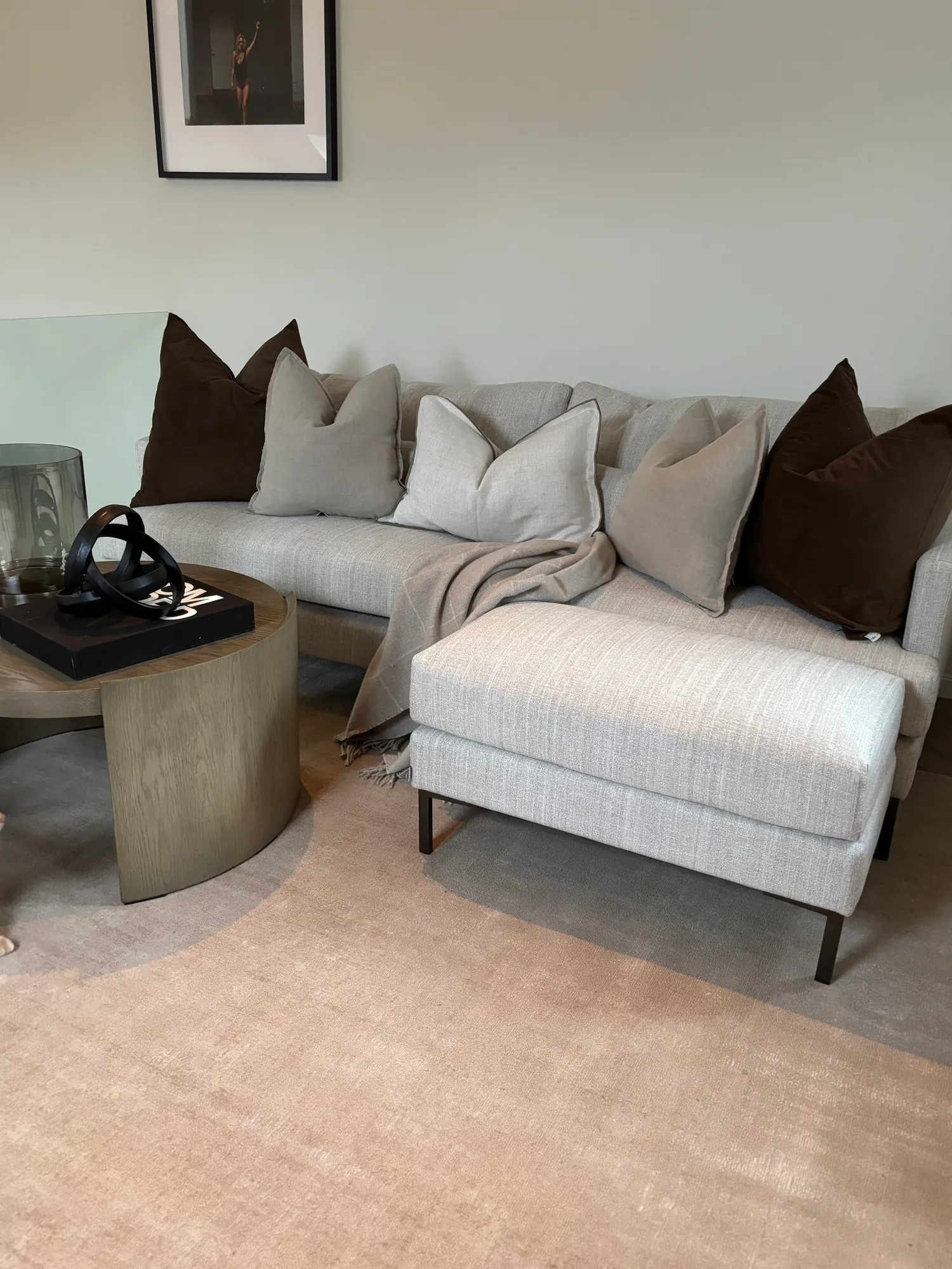 Lys sofa med puter i brunt og beige ved et rundt sidebord