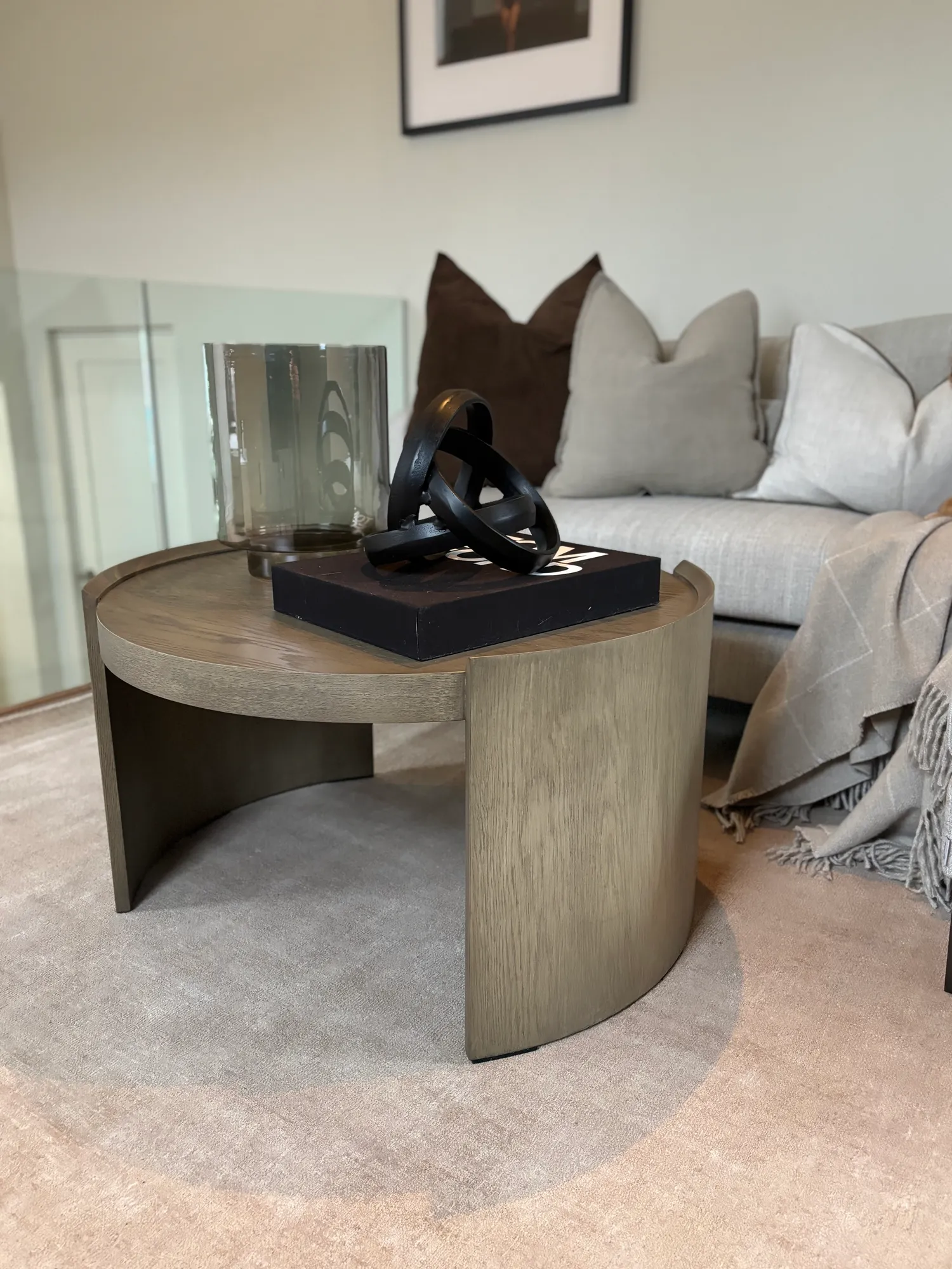 Rundt sidebord i tre med sort skulptur foran sofaen