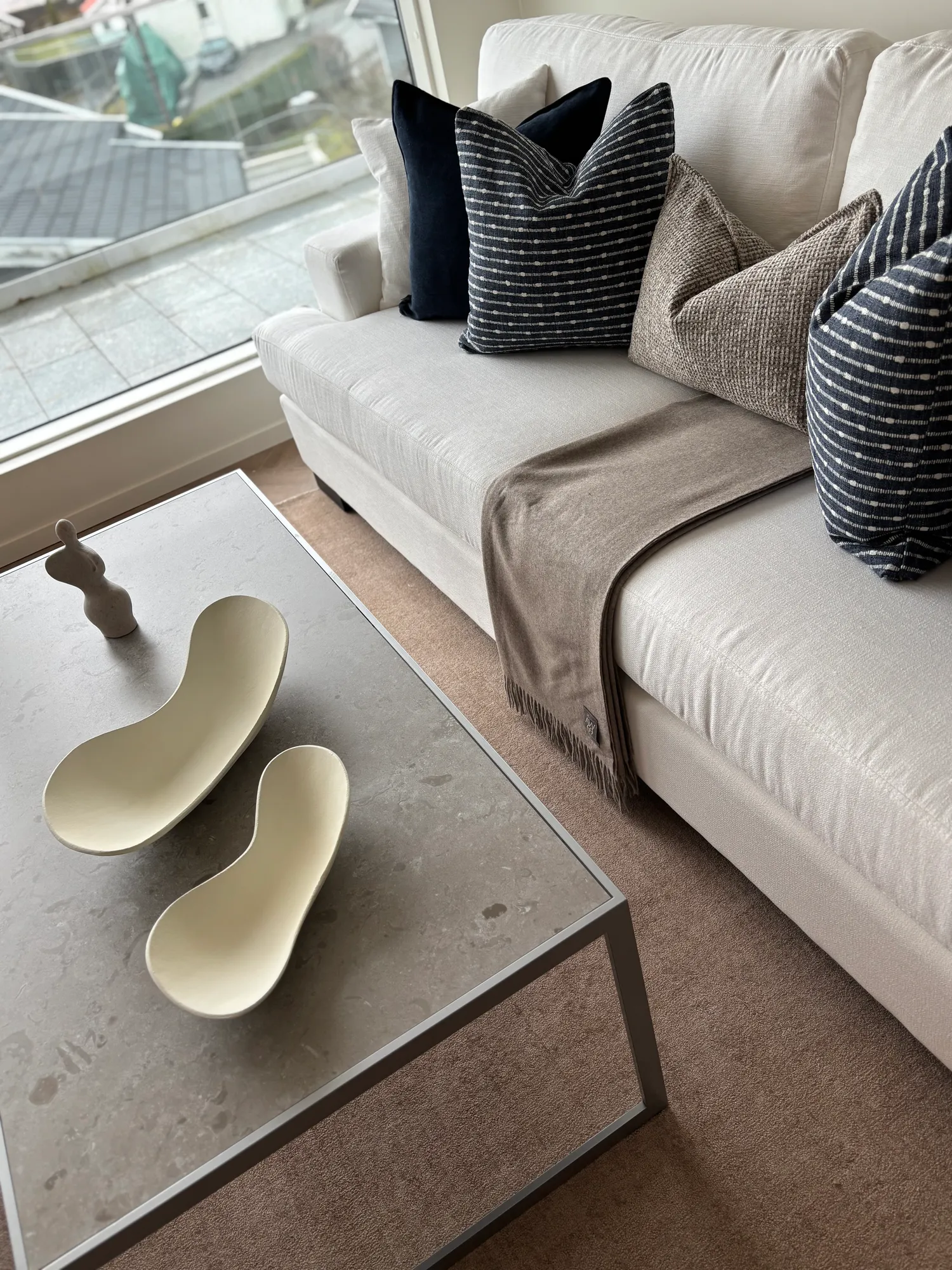 Sofabord i stein med lyse keramikkfat foran hvit sofa