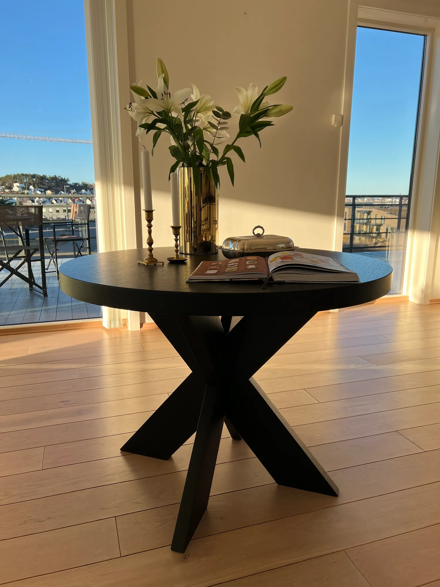 Rundt, sort bord med liljer foran vinduer mot sjøen
