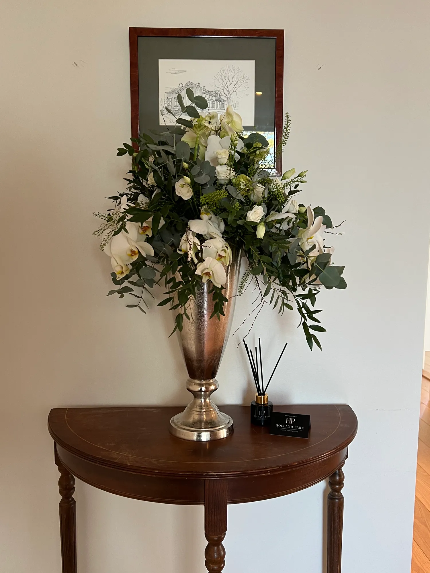 Halvmånebord i mørkt tre med stor blomsteroppsats i sølvvase
