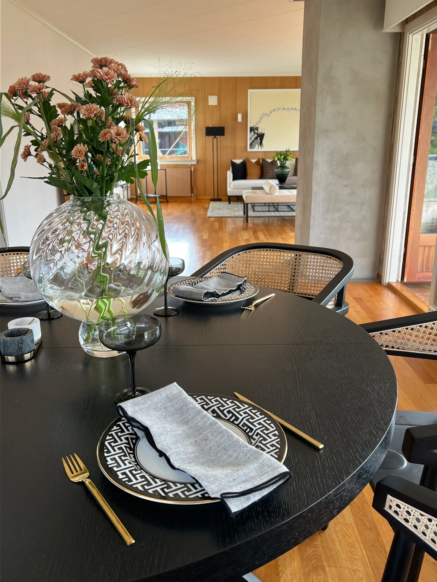 Dekket, sort spisebord med blomster i glassvase, stuen i bakgrunnen