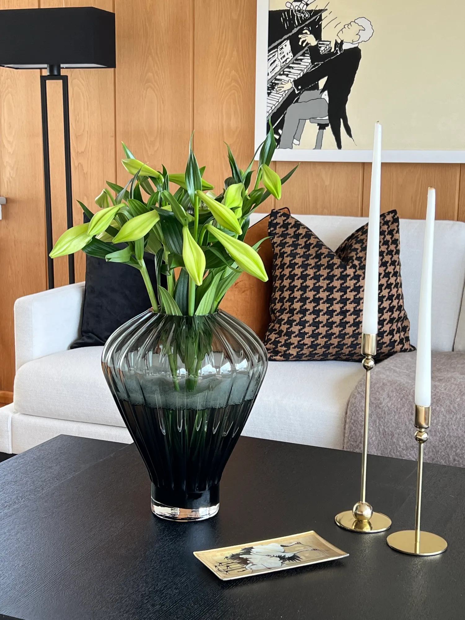 Glassvase med liljer og lysestaker i messing på sort sofabord