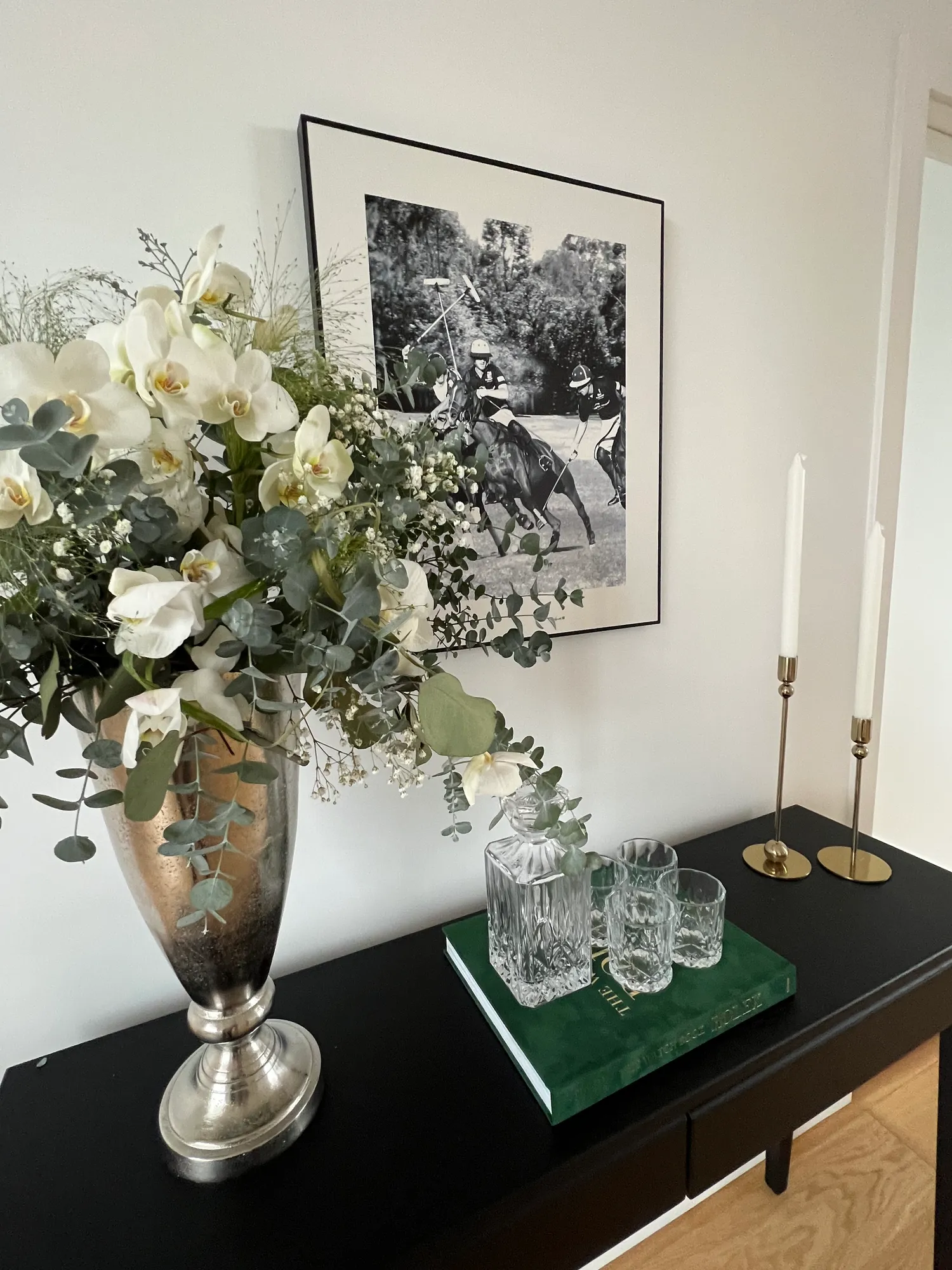 Konsollbord med blomster i sølvvase, krystallglass og lysestaker