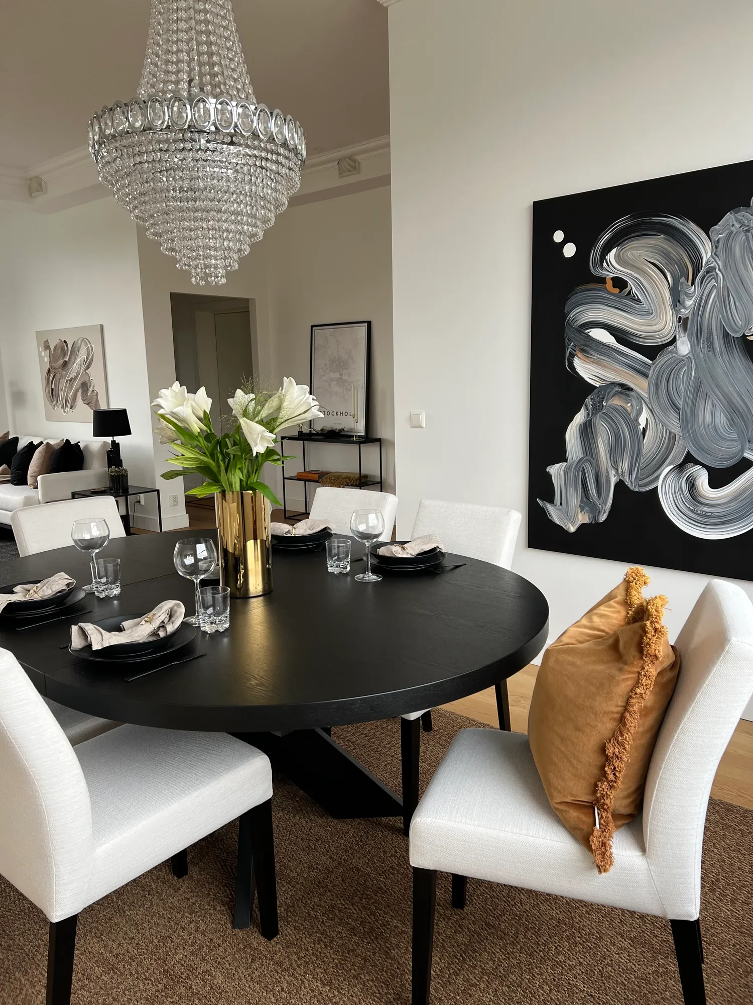 Spisestue med rundt, sort bord, hvite stoler og krystallkrone