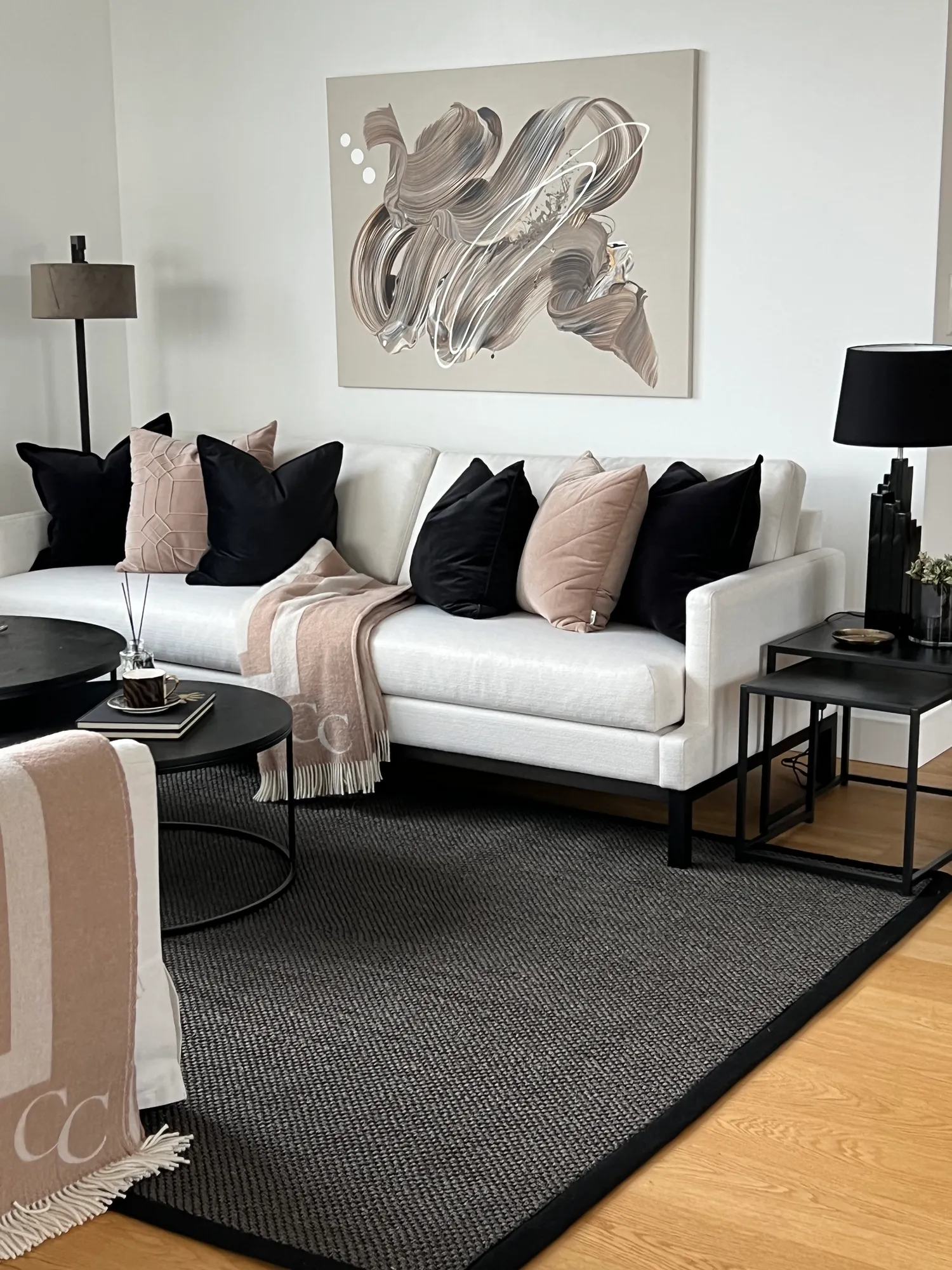 Hvit sofa med puter i sort og rosa under et abstrakt maleri