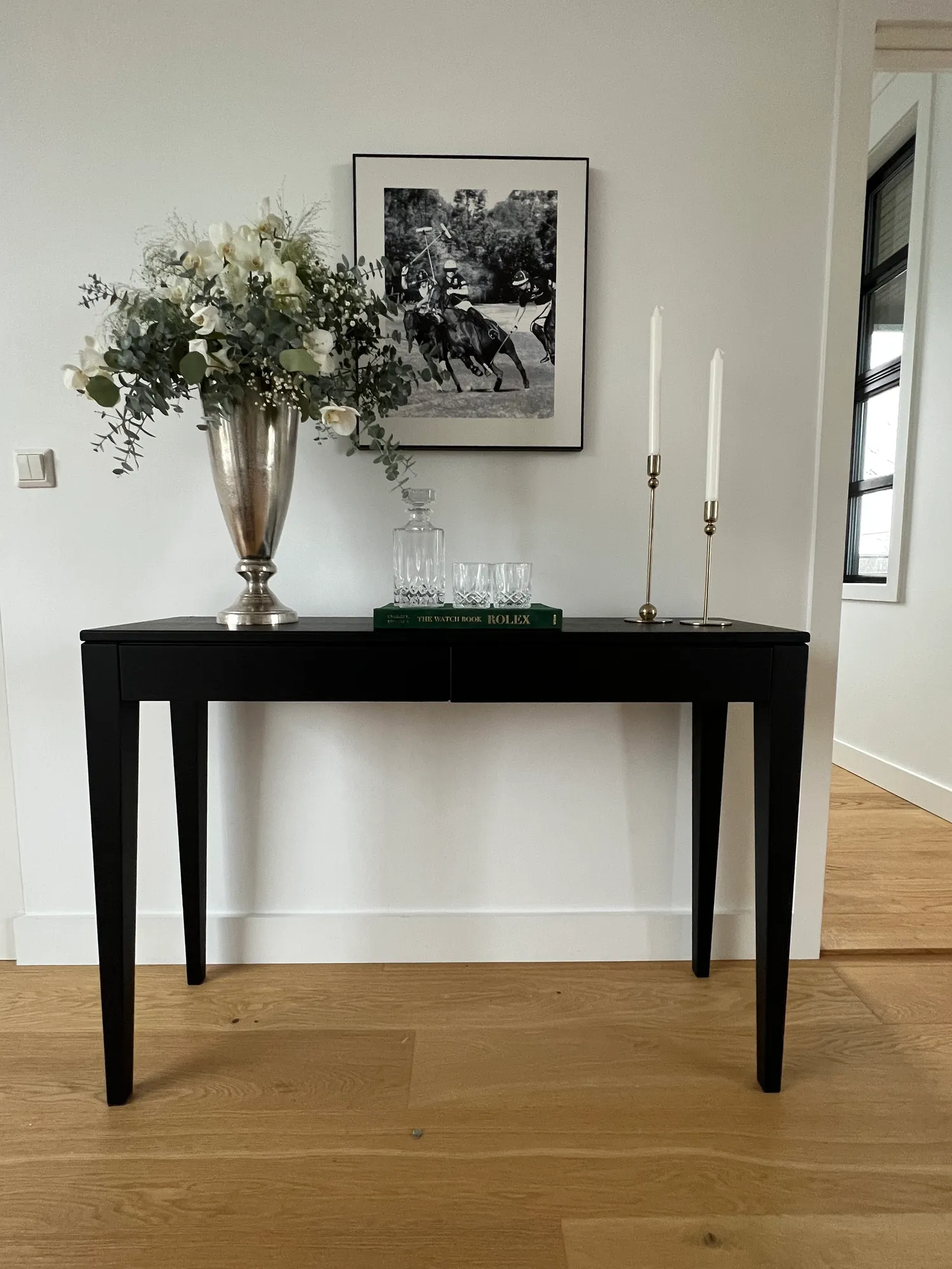 Sort konsollbord med blomster, lysestaker og fotografi i sort ramme